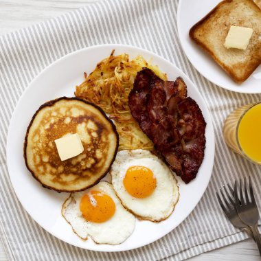 Beyaz ahşap bir masada, tam Amerikan Pastırmalı Kahvaltı, Hash Browns, Yumurta ve Krepler. Dümdüz, tepeden, yukarıdan. 