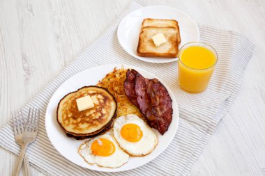 Beyaz ahşap bir yüzey üzerinde tam Amerikan Kahvaltısı, Hash Browns, Yumurta ve Krepler, yan manzara.