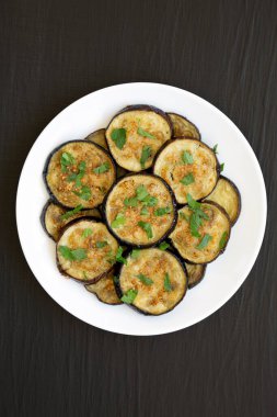 Siyah bir yüzey üzerinde beyaz bir tabakta ev yapımı organik fırınlanmış patlıcan. Dümdüz, tepeden, yukarıdan.