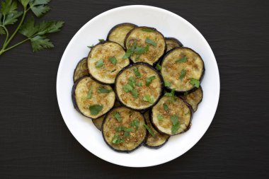 Siyah arka planda beyaz bir tabakta ev yapımı organik fırınlanmış patlıcan. Dümdüz, tepeden, yukarıdan. 