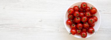 Beyaz ahşap arka planda bir kasede taze kırmızı organik kiraz domatesleri, üst manzara. Dümdüz, tepeden, yukarıdan. Boşluğu kopyala.