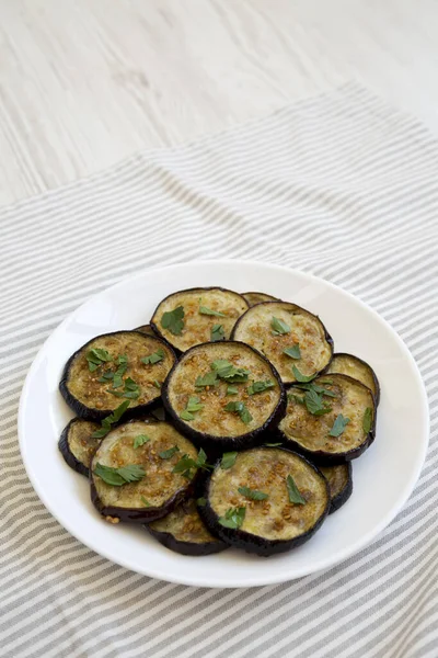 Beyaz ahşap arka planda beyaz bir tabakta ev yapımı organik fırınlanmış patlıcan. Boşluğu kopyala.