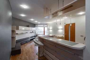 Lüks dairedeki mutfak ve oturma odasının modern iç mekanı. Hafif ahşap tezgahlı yeni mutfak seti. Tahta kapılar. Bar taburesi.