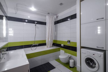 Lüks dairede modern banyo. Beyaz, yeşil ve siyah fayanslar. Lavabo ve ayna. Tuvalet ve banyo. Çamaşır makinesi. Beyaz dolaplar.