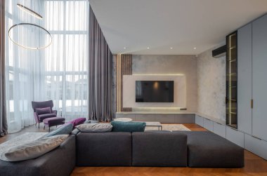 Lüks bir dairede modern bir oturma odası. Yastıklı rahat bir kanepe. Duvarda televizyon var. Panoramik pencere.