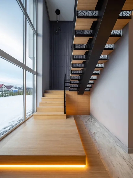 Lüks özel evin modern iç mimarisi. Aydınlatmalı tahta merdiven. Panorama penceresi.