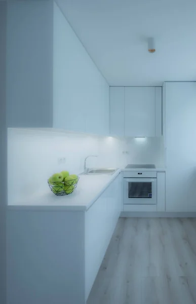 Interior dapur yang terang di apartemen studio mewah. Lantai parket. Dapur putih dengan wastafel, oven dan kulkas. Apel hijau. — Stok Foto