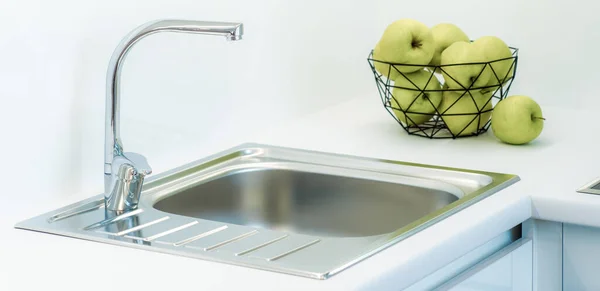 Close-up of sink and green apples in vase on white counter of kitchen set. — Stock Photo, Image