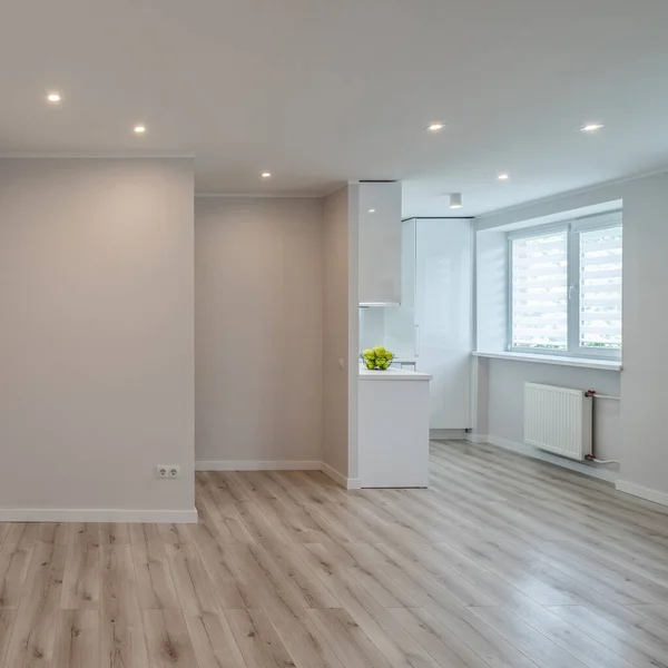 Modern light interior of renovated studio apartment without furniture. Empty living room and white kitchen. Apples in bowl. — Stock Photo, Image