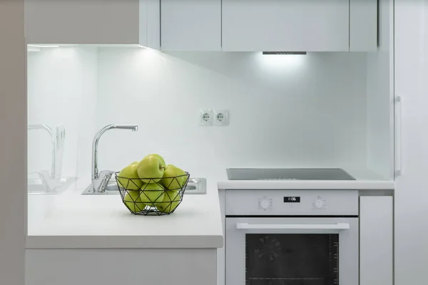 Elegante juego de cocina blanca. Manzanas verdes en jarrón en el mostrador. Horno. Fregadero y fauce. — Foto de Stock