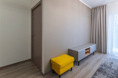 Tarafsız tonlarda modern iç mekan. Sarı yastıklı tabure. Ahşap ayakta.