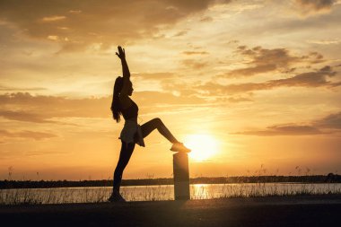 Siluet Genç kadın gün batımında plajda meditasyon yogası yapıyor.