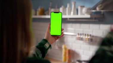 Green Mock-up Screen ile Smartphone kullanarak Kanepede uzanan, Swiping, Scrolling Jestleri yapan kadın. Kız Cep Telefonu Kullanıyor, İnternet Sosyal Ağ Taraması. Bakış açısı çekimi. Mutfak.