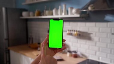 Green Mock-up Screen ile Smartphone kullanarak Kanepede uzanan, Swiping, Scrolling Jestleri yapan kadın. Kız Cep Telefonu Kullanıyor, İnternet Sosyal Ağ Taraması. Bakış açısı çekimi. Mutfak.