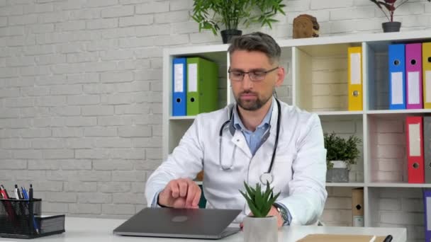 Zdalny lekarz nosi biały płaszcz medyczny w gabinecie szpitalnym otwiera za pomocą laptopa — Wideo stockowe