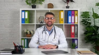 Hastane ofisindeki gülümseyen doktor hastayı internetten selamlıyor.