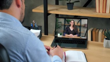 Konferans videosuyla çalışan öğrenci bilgisayarı, not defterine yazıyor.
