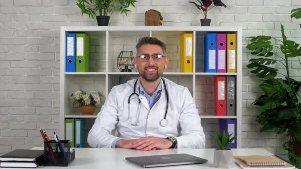 Médico sorridente no escritório do hospital saúda paciente laptop videocall on-line — Vídeo de Stock