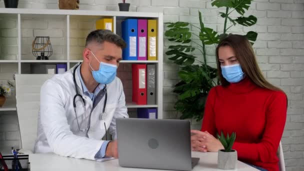 Doctor in white coat shows tells patient causes of health problems on laptop — Stock Video