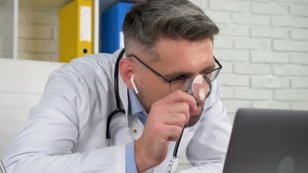 Doctor looks magnifying glass, diagnoses patient online video call laptop webcam — Stock Video