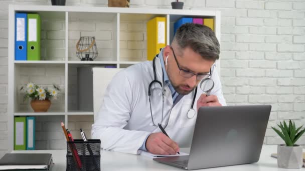 Dokter in het ziekenhuis kantoor ziet vergrootglas schrijft diagnose in notebook — Stockvideo