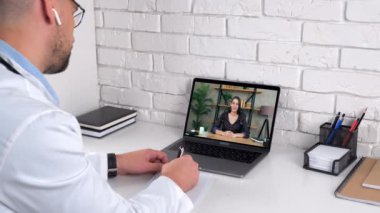 Hastane ofisindeki erkek doktor semptomları not defterine yazar hasta müşterisini dinler.