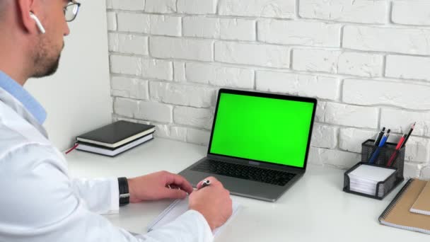 Médecin dans le bureau de l'hôpital regardant l'ordinateur portable à écran vert écoute parler patient — Video