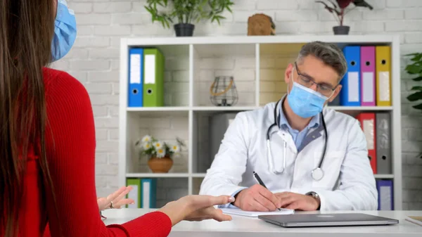 Doctor wear protective mask writes symptoms in notebook focused listens patient