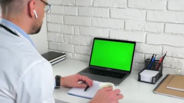 Doktor yeşil ekran dizüstü bilgisayarı kahve içen hastayı dinliyor.