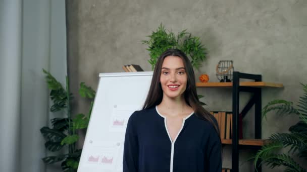 Lachende aantrekkelijke vrouw business coach op zoek camera op achtergrond whiteboard — Stockvideo
