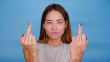 Gri tişörtlü kadın gülümser, dans eder, mavi arka planda orta parmağını gösterir.