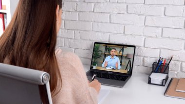 Evde çalışan kız öğrenci videosu laptopunu arıyor, not defterine görev yazıyor.