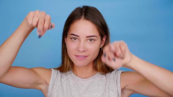 Αστεία γυναίκα με γκρι μπλουζάκι χαμογελά χοροί δείχνει μεσαίο δάχτυλο σε μπλε φόντο — Αρχείο Βίντεο