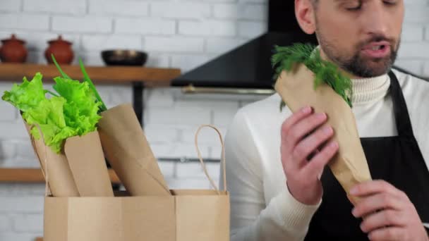 エプロンのシェフは、台所で食べ物を準備するために紙袋から野菜を削除します — ストック動画