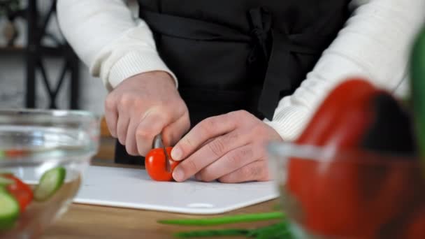 Chef kok man in zwarte schort gesneden verse cherry tomaat aan boord in huis keuken — Stockvideo