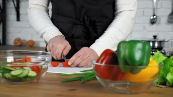 Chef hombre en delantal negro en rodajas de tomate cherry fresco a bordo en la cocina casera — Vídeos de Stock