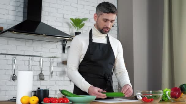 エプロンの男シェフは台所で主婦料理サラダオンラインビデオ通話を教えています — ストック動画