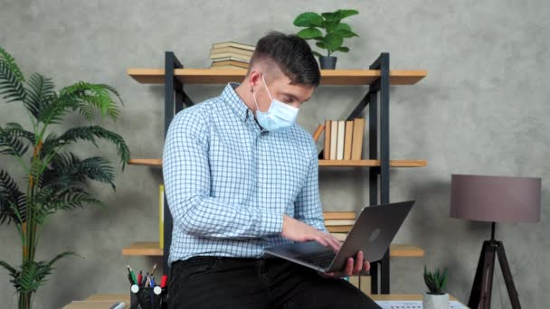 Businessman in protective medical mask on face sits at desk in office use laptop — Stock Video