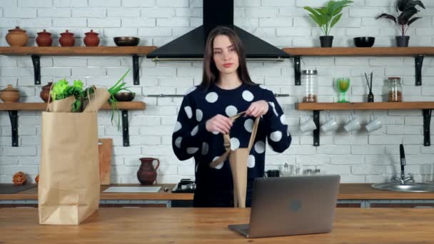 Dona de casa vem para cozinha coloca no avental preparar estudo webinar on-line no laptop — Vídeo de Stock
