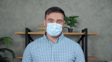 Yüzünde tıbbi maske olan gülümseyen iş adamı yüzünü kameraya çeviriyor.