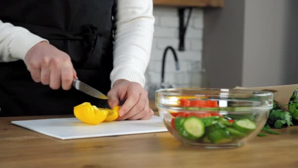 Chef hombre en delantal negro en rodajas de pimiento amarillo fresco a bordo en la cocina casera — Vídeos de Stock