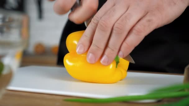 Primer plano manos chef hombre en delantal cortes fresco pimiento amarillo a bordo en la cocina — Vídeos de Stock