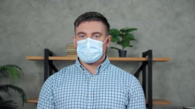 Yüzünde tıbbi maske olan ciddi bir iş adamının yüzünü kameraya çeviriyor.