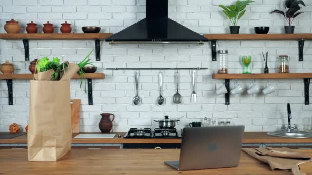 Fartuch Laptop i torba papierowa ze świeżymi warzywami stoi na stole w kuchni domowej — Wideo stockowe