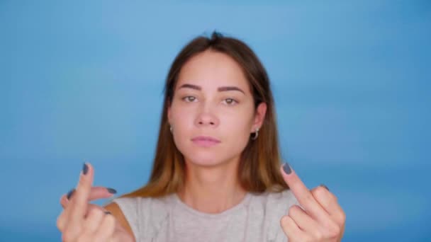 Смішна жінка в сірих футболках танцює, показує середній палець на синьому фоні — стокове відео