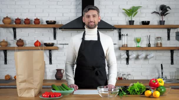 Πορτρέτο χαμογελαστός γενειοφόρος άνδρας με μαύρη ποδιά ψάχνει κάμερα στο σπίτι κουζίνα — Αρχείο Βίντεο