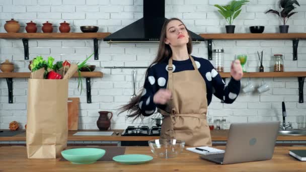 Забавная красивая женщина домохозяйка в бежевом фартуке танцует поет на домашней кухне — стоковое видео