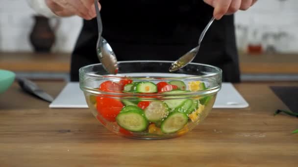 Chef de pie cerca de la mesa de la cocina mezcla ensalada vegetariana con cucharas en tazón de vidrio — Vídeos de Stock