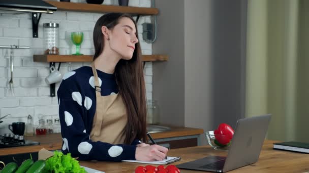 Huisvrouw luisteren chef-kok schrijft culinair recept in notebook studie online in de keuken — Stockvideo