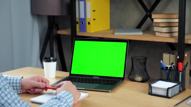 Бизнесмен в офисе сидит на стуле за столом рассказывает с зеленым экраном ноутбука — стоковое видео